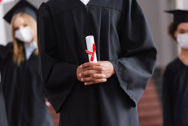 Vista ritagliata di studente afro-americano in abito accademico in possesso di diploma  - Foto, immagini