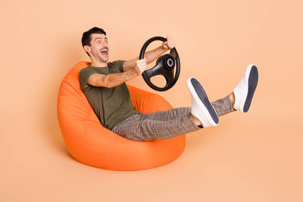 Full size photo of young handsome crazy smiling sit armchair riding fast hold steering wheel isolated on pastel color background - Фото, зображення
