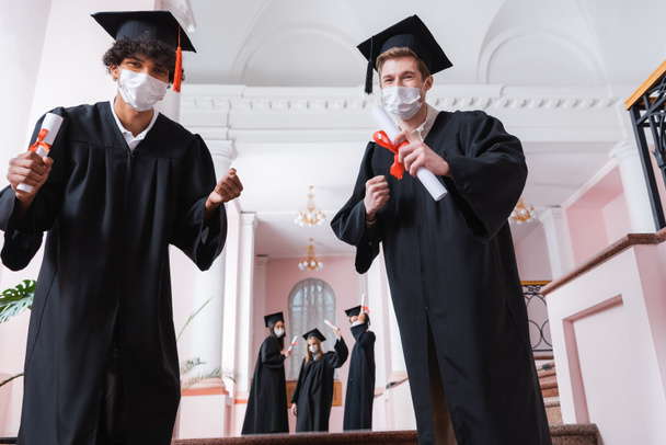 Monietniset poikamiehet lääketieteellisissä naamioissa, jotka osoittavat kyllä-elettä yliopiston salissa  - Valokuva, kuva