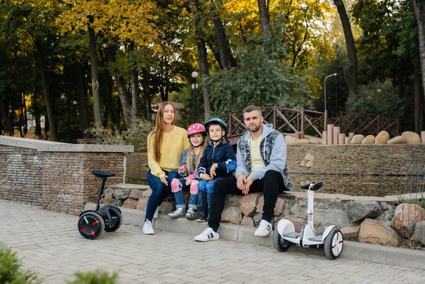A large happy family rides Segways and electric scooters in the Park on a warm autumn day during sunset. Family vacation in the Park. - Фото, изображение