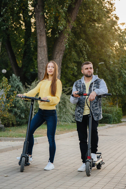A young beautiful couple rides electric scooters in the Park on a warm autumn day. Hobbies and recreation. - Valokuva, kuva