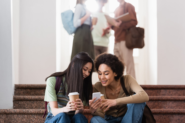 Studenti multietnici sorridenti con il caffè per andare con il cellulare  - Foto, immagini