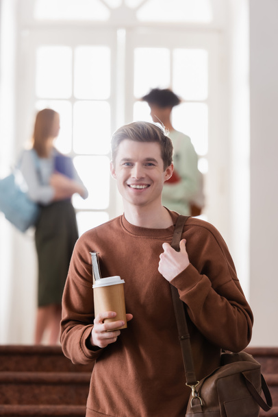 Cheerful student holding bag, notebook and paper cup  - Фото, зображення