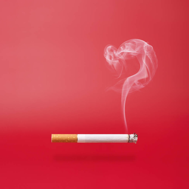 Fumo come punto interrogativo e una sigaretta fumante su sfondo rosso con spazio di copia. - Foto, immagini