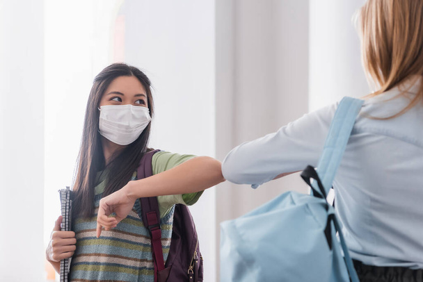 Asian student in medical mask doing elbow bump with friends in university  - Photo, Image