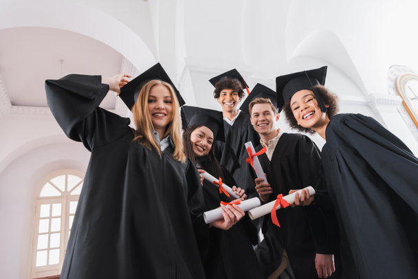 Low angle view of multiethnic graduates with diplomas smiling at camera  - Photo, Image