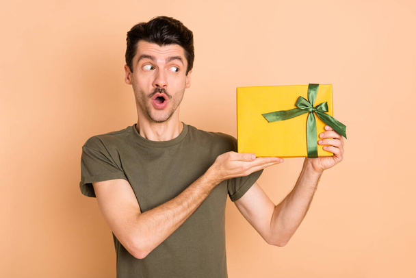 Photo portrait of man surprised looking keeping wrapped festive gift box isolated on pastel beige color background - Foto, Bild