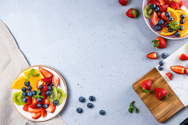 Fresh summer salad of various fruits and berries. Kiwi, orange, strawberry and blueberry on a plate decorated with mint on a table top view, free space for text - Foto, afbeelding