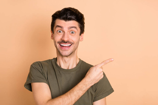 Photo portrait of guy smiling pointing finger at empty space overjoyed isolated on pastel beige color background - Φωτογραφία, εικόνα