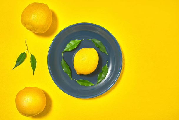whole yellow lemons with leaves on the table on a blue plate - Fotó, kép