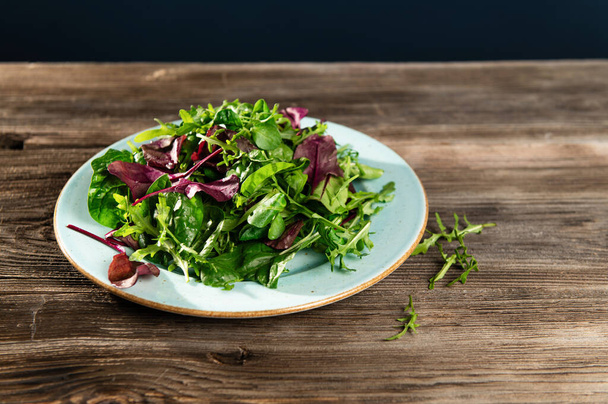 salad mix of fresh herbs, arugula, Swiss chard, spinach in tarenle on a wooden background, top-side view - Photo, Image