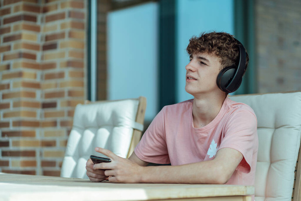 fiatal barna hajú tinédzser fülhallgatóval és okostelefonnal a kezében - Fotó, kép