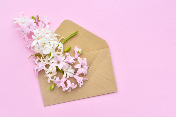 ピンクの背景にヒヤシンスの花が入った封筒。フラットレイアウト、トップビュー. - 写真・画像