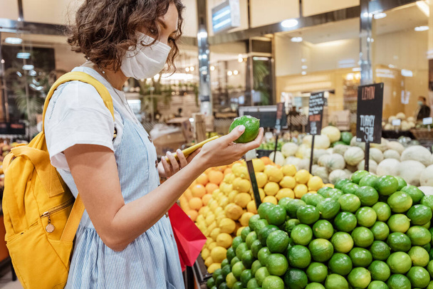 Donna cliente indossando maschera viso, shopping e raccolta di lime e frutta al limone nel supermercato negozio di alimentari - Foto, immagini