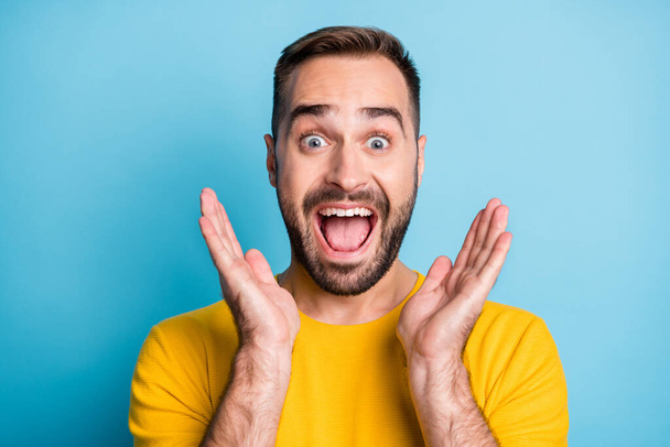 Photo of young crazy excited happy smiling cheerful man in yellow t-shirt see big sale isolated on blue color background - Foto, immagini