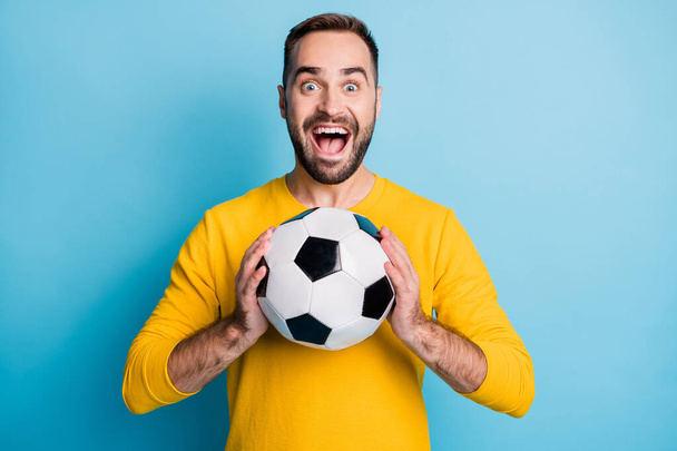 Photo of young excited crazy happy positive smiling cheerful man hold football ball in hands isolated on blue color background - Foto, immagini