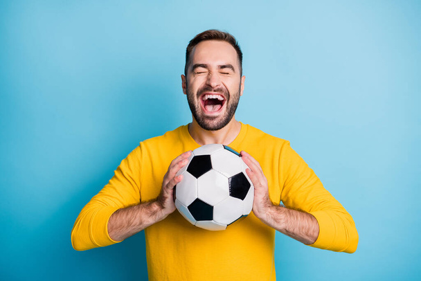 Photo portrait of amazed cheerful man keeping football ball shouting isolated on vibrant blue color background - Foto, afbeelding