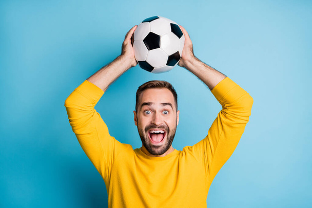 Photo of young crazy happy positive excited cheerful man hold football ball above head isolated on blue color background - Photo, Image