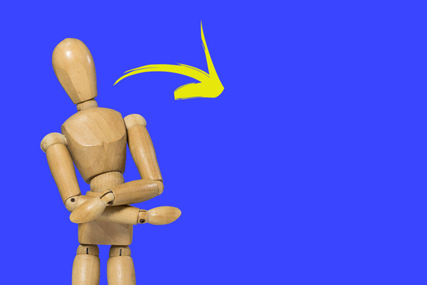 Muñeca figura de madera pose en gesto de brazos cruzados sobre fondo colorido y flecha amarilla con espacio para escribir - Foto, imagen