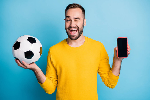 Photo portrait of man with ball smiling showing touchscreen of cellphone winking isolated on vivid blue color background - Fotoğraf, Görsel