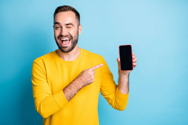 Photo portrait of man pointing finger display of smartphone copyspace winking isolated on vibrant blue color background - Φωτογραφία, εικόνα