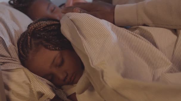 Encerrada de adorable niñita africana durmiendo en la cama, mano de padre irreconocible cubriéndola con manta y palmaditas en la cabeza - Imágenes, Vídeo
