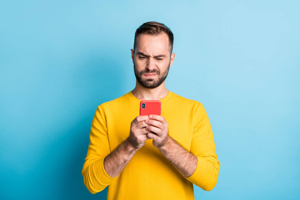 Photo of young unhappy upset sad unsure uncertain man see dislike bad comment in phone isolated on yellow color background - Fotografie, Obrázek