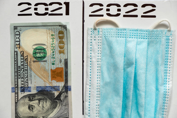 2021 und 2022 in Stift über einer Spalte in zwei separaten Spalten geschrieben, Dollar und eine medizinische Maske, Untersumme, Gesundheit - Foto, Bild