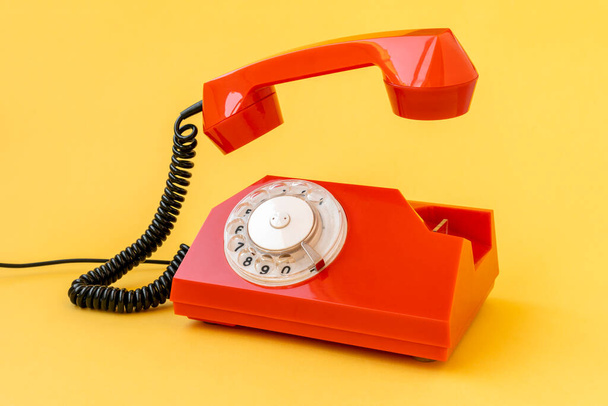 Retro orange telephone with the receiver raised, isolated on yellow background - Photo, Image