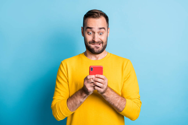 Photo of young handsome shocked amazed surprised man see unexpected news in phone isolated on blue color background - Foto, Imagen