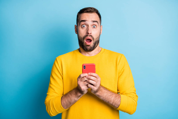 Фотографічний портрет шокованого студента, який дивиться, тримаючи мобільний телефон відкритим ненависником рота, не схожим на ізольований на яскраво-блакитному фоні
 - Фото, зображення