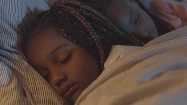 Nahaufnahme eines entzückenden kleinen afrikanischen Mädchens mit Zöpfen, das im Bett schläft, während ihre Schwester hinter ihr liegt - Filmmaterial, Video
