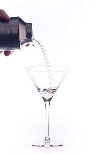 Πιτσιλιές σε ένα ποτήρι κοκτέιλ. Ο άνθρωπος σερβίρει ένα κοκτέιλ τζιν σε ένα ποτήρι σε λευκό φόντο - Φωτογραφία, εικόνα