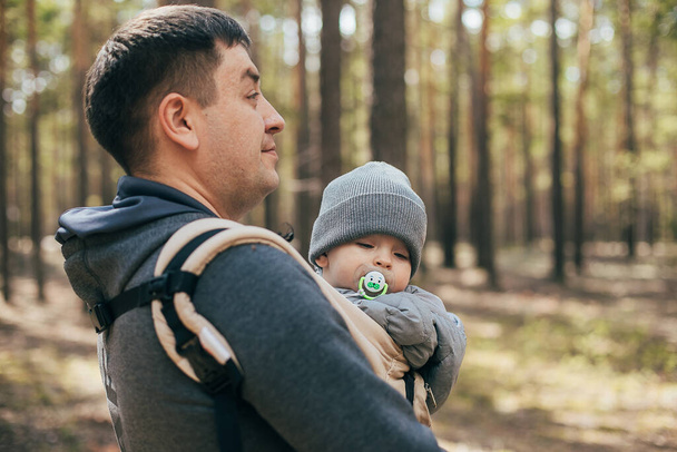 Father carrying his baby boy in ergo bag. Lifestyle, authentic moment. Concept of togetherness, care, parent love. - Zdjęcie, obraz