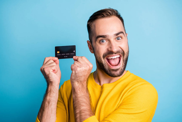 Photo of young handsome excited crazy smiling cheerful man showing credit card isolated on blue color background - Fotoğraf, Görsel