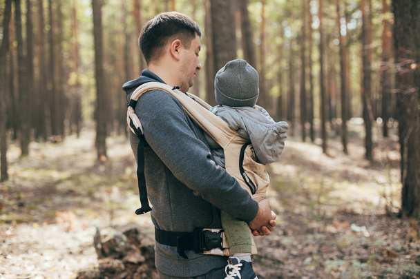 Father carrying his baby boy in ergo bag. Lifestyle, authentic moment. Concept of togetherness, care, parent love - Photo, Image
