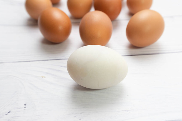 bílé vejce s přední mnoho vejce na bílém stole dřevěné pozadí. kuřecí vejce uvnitř kachní vejce nebo různé lidské v sociální nebo jiné obchodní koncepce. Selektivní zaměření. - Fotografie, Obrázek