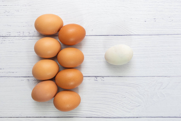 Önünde bir sürü yumurta olan beyaz yumurta beyaz masa ahşap arka planda. Ördek yumurtasının içindeki tavuk yumurtası ya da sosyal ya da iş dünyasındaki farklı bir insan. Seçici odaklanma. Yalnız Yaşam konsepti. - Fotoğraf, Görsel