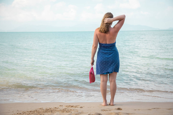 una mujer sostiene en su mano una bolsa de compras de malla y se encuentra en el borde del mar en una playa de arena. concepto de ecología. consumo consciente - Foto, imagen
