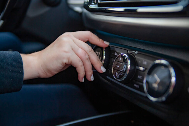 το χέρι μιας γυναίκας γυρίζει το κουμπί για την προσαρμογή του συστήματος ελέγχου του κλίματος σε ένα σύγχρονο premium αυτοκίνητο. ρύθμιση μια άνετη θερμοκρασία στο αυτοκίνητο. ταξιδεύουν με το αυτοκίνητο. Χωρίς πρόσωπο. - Φωτογραφία, εικόνα