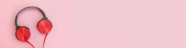 Красные наушники на розовом фоне. Минималистская простая фотография наушников с копировальным пространством, баннером. Красные диджейские наушники с кабелем, изолированным на цветном заднем плане, плоский вид сверху. Концепция музыки - Фото, изображение