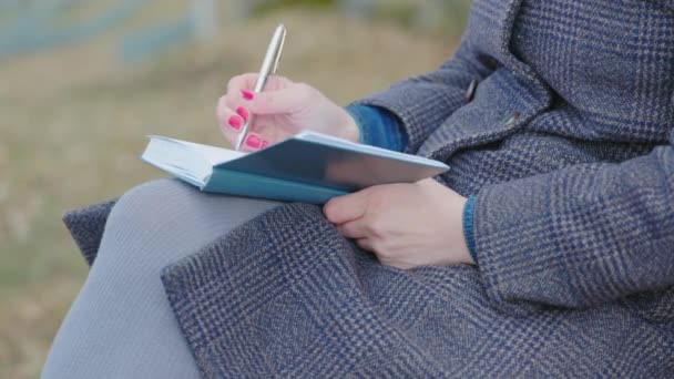 Een vrouw schrijft op haar dagboek in het park op de bank. - Video