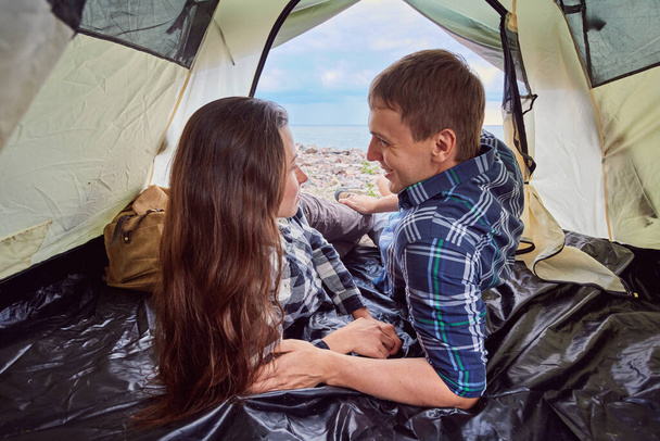 二人でキャンプ。テントの中で景色を眺めながら座っている若者たち - 写真・画像
