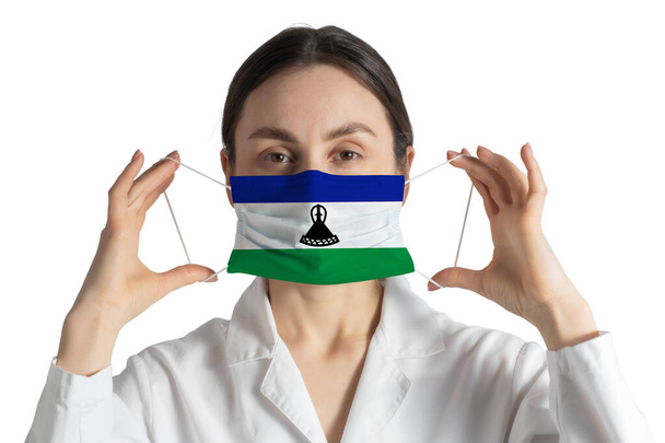 Respirator with flag of Lesotho Doctor puts on medical face mask isolated on white background. - Photo, Image