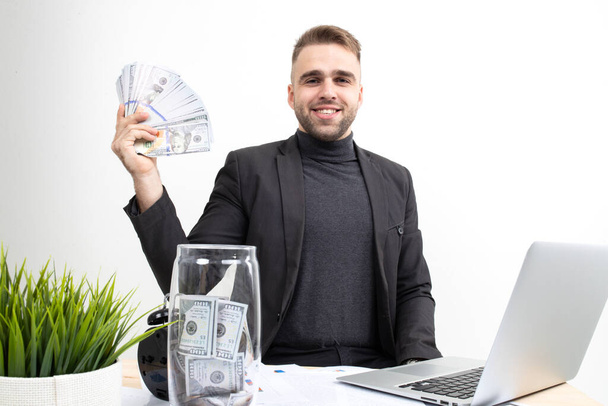 A guy with business clothes shows the earnings while sitting at the workplace - Foto, Bild