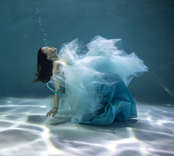 gyönyörű lány egy báli ruha fehér és kék ruha egy kék háttér víz alatt  - Fotó, kép