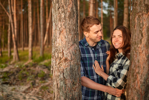 fiatal pár mosolyog egymásra egy romantikus randin az erdőben - erős napfény - lövés a nap ellen - Fotó, kép