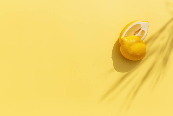 Twee gehalveerde stukken citroen met schaduw van palmblad op gele achtergrond. Gezond eten, reizen of vakantie concept - Foto, afbeelding