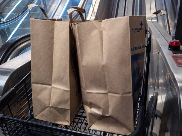 Seattle, WA USA - circa April 2021: View of a shopping cart exiting the cart escalator inside a QFC grocery store, filled with bags of groceries. - Photo, image