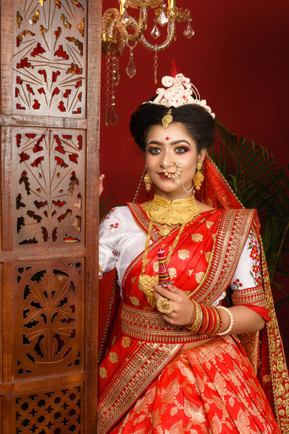 Stunning Indian bride dressed in red traditional Banarasi sari embroidered with gold jewellery and bangles holding gach kouto or sindoor box in hand, Wedding symbol sindoor box. Wedding fashion. - Photo, Image